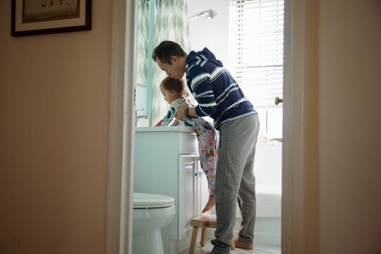 Father carrying daughter washing hands in bathroom sink seen through doorway at home