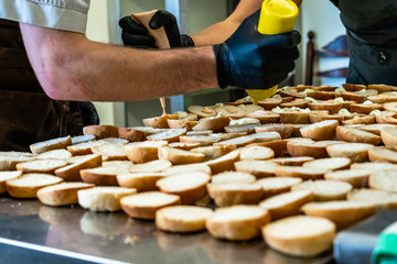 Female and Male Chef Putting Ingredients of Burgers on a Sliced Bread Spread on a Table in Black Gloves - Concept of the Hard Working Person and the Hygiene in the Kitchen