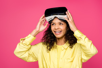happy curly african american woman wearing virtual reality headset and smiling isolated on crimson