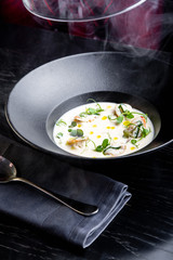 Cream soup is steaming in a black plate with on the black table. Photo for menu