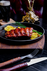 Close up Gourmet Main Dish with Grilled Pork Rib and Fried Potatoes on Black pan. Served on Wooden Board