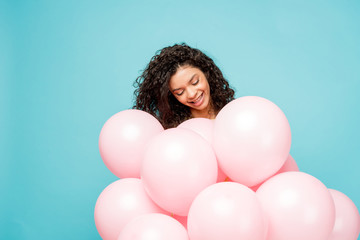 attractive curly african american girl looking at pink air balloons isolated on blue