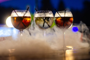 Beautiful row line of different colored alcohol cocktails on a party, martini, vodka,and others on decorated catering bouquet table on open air event, picture with beautiful bokeh