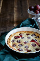 Plum cotage cheese tart with icing sugar in green napkin with fresh plums on the background