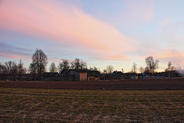 Field with village houses on the horizon at sunset in the spring against the beautiful evening sky