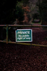 Fototapeta premium Private no right of way sign on old rusty metal gate blocking access to woodland countryside track with shallow depth of field