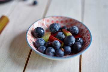 Blueberries with rhubarb in a bowl on a wooden table with rhubarb next to the bowl