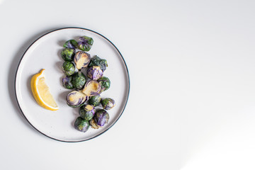 Healthy food concept, dieting, vegetarian, vegan - organic purple brussel sprouts fried on plate with lemon, top view
