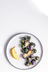 Healthy food concept, dieting, vegetarian, vegan - organic purple brussel sprouts fried on plate with lemon, top view