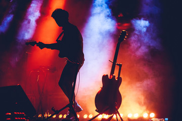Guitarist on a stage playing rock to the crowd of people. Musician plays an acoustic guitar during...