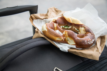 Deutsche Schnittlauchbrezel Brezel mit Schnittlauch, Butter und Frischkäse auf Bäckertüte und Koffer als Snack für Reisen und unterwegs