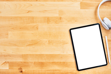 Digital tablet with blank white screen, pen and wireless headphone on wooden office desk. Top view. Copy space for text or design. Flat lay.
