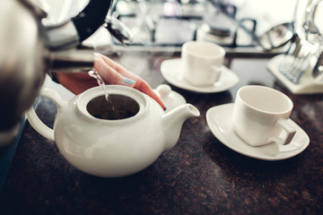 Woman pouring tea into ceramic cup at table