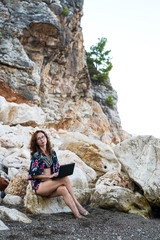 Woman workaholic working on a laptop while sitting on a stone on the beach.