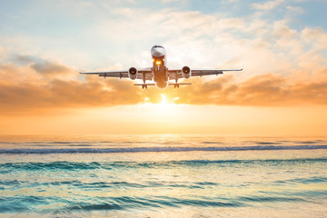 Fototapeta na wymiar Airplane flies over the green ocean during landing at sunset.