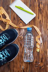 Healthy lifestyle and sports background. Sports shoes, Notepad and pen, and water bottle on wooden background with copyspace, topview.