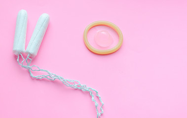 tampon and condom on pink isolated background