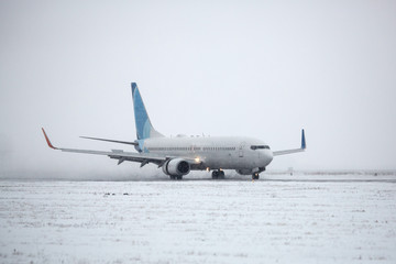 Fototapeta na wymiar Airliner on runway in blizzard. Aircraft during taxiing on landing strip during heavy snow. Passenger plane in snow at airport.