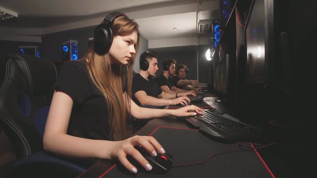 Beautiful female gamer wearing headset, playing in online video game with another people sitting in line beside in club. eSport Cyber Games Internet