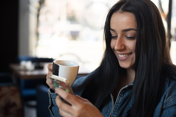 young woman enjoying in coffee and holding cellphone 