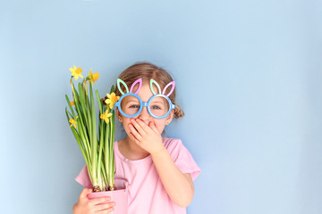 Cute little child wearing bunny ears glasses and holding flowers on Easter day. Easter girl portrait, funny emotions, surprise. Copyspace for text.