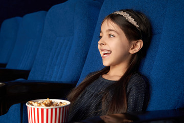 Joyful little girl watching movie, laughing in cinema.