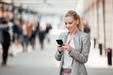 Beautiful smiling businesswoman using smartphone on the city street.
