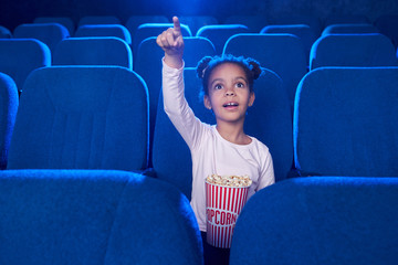 Cute girl poiniting with finger at screen in cinema.