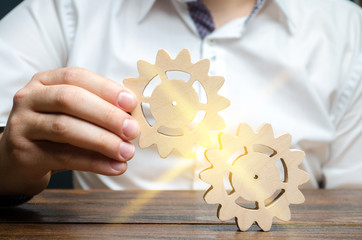 Businessman in white shirt connects two wooden gears. Symbolism of establishing business processes...