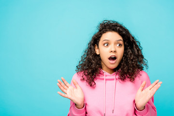 shocked curly african american girl standing isolated on blue
