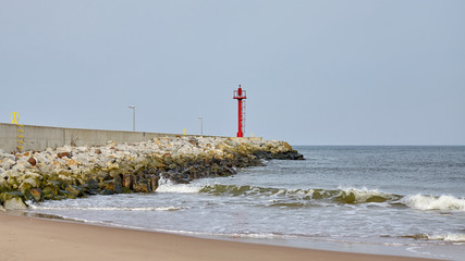 Red beacon on a concrete quay seen from a beach.
