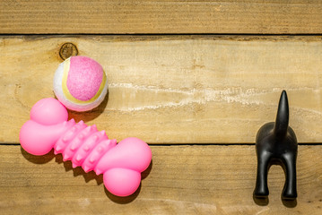 Tight shot of pink dog toys and black dog butt leash holder on rustic wooden background.