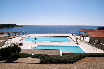 Swimming pools of luxury holiday hotel, amazing nature view landscape sea. Relax near two swimming pools with handrail, deck chairs, sun loungers and parasols waiting for tourists in tropical resort.