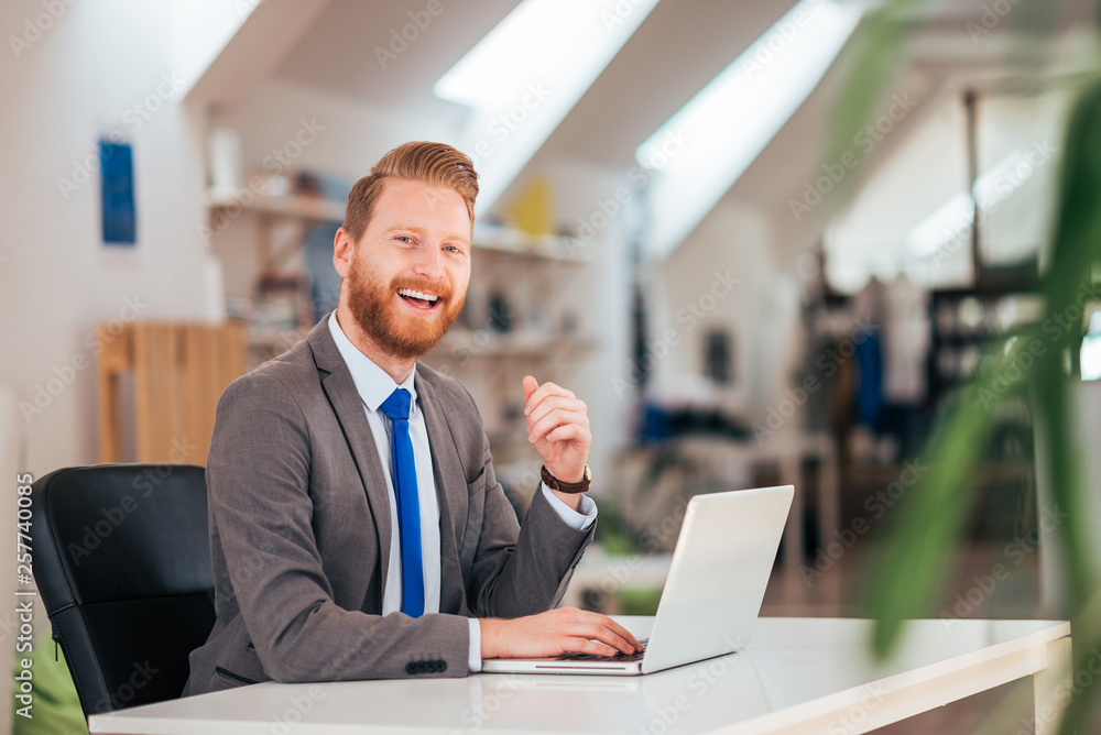 Wall mural Smiling ginger businessman in formal wear at office desk.