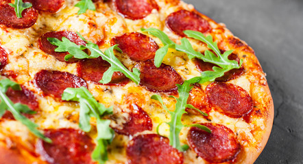 Pepperoni Pizza with Mozzarella cheese, salami, Tomato sauce, pepper, Spices and Fresh arugula. Italian pizza  on Dark grey black slate background