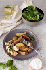 Baked potatoes sliced ​​with chicken fillet in a creamy sauce in a plate on the background of a salad bowl with spinach and a glass of water and lemon.
