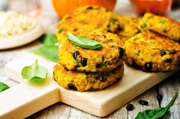 black bean millet pumpkin burgers with spinach leaves on a wood background