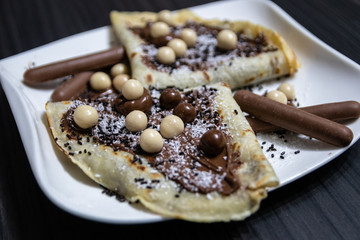 Homemade pancakes with chocolate, chocolate crumbs and candies on white plate