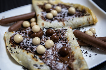 Homemade pancakes with chocolate, chocolate crumbs and candies on white plate