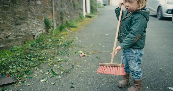 Little toddler sweeping leaves in the street