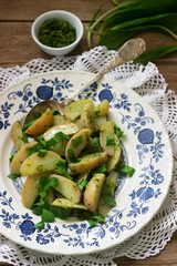 Vegetarian potato salad with wild garlic and pesto sauce on a wooden background. Rustic style.