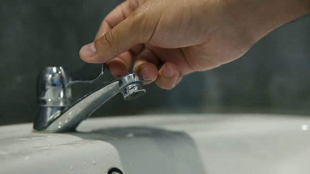 Slow motion - turning water on, water flows from the tap, close up of bathroom sink.