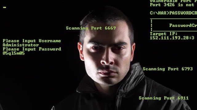 Hacker looking into the camera lens in a dark environment. Green coding appearing on the screen showing the hacking process.