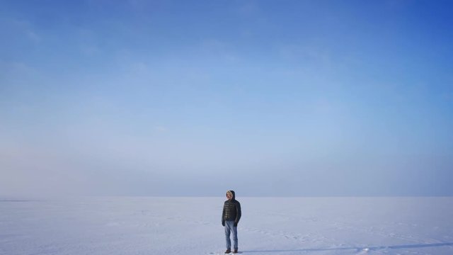 Zooming in shot of middle-aged explorer watching smilingly into camera on snow desert background.