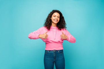 happy curly african american girl showing thumbs up isolated on blue