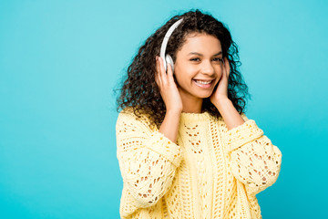 Fototapeta premium happy curly african american girl listening music in headphones isolated on blue