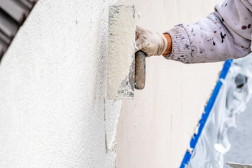 Construction worker plastering and smoothing concrete wall with cement