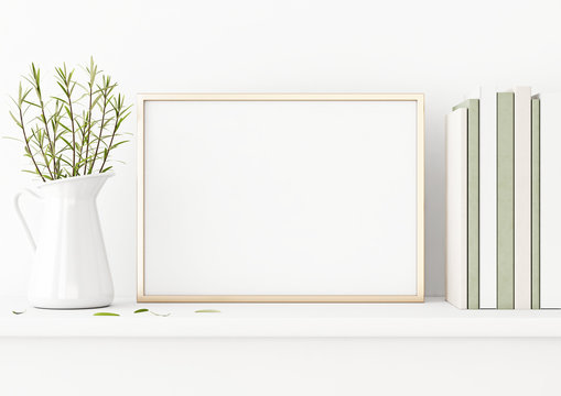 Horizontal poster mockup with golden metal frame standing on table and decorated with jug, green plants and pile of books on empty white wall background. 3D rendering, illustration.