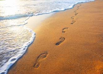 beach, wave and footprints at sunset time