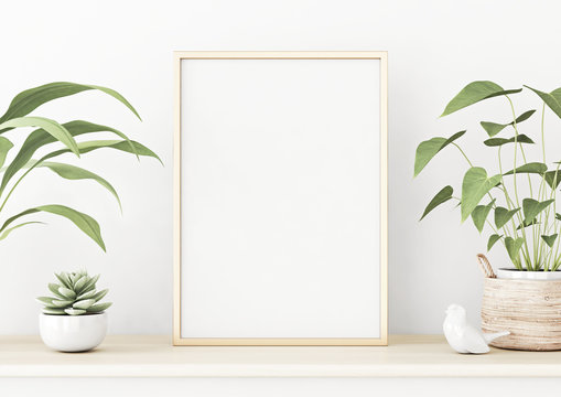 Vertical poster mockup with golden metal frame standing on wooden table and decorated with succulent and green plants in basket on empty white wall background. 3D rendering, illustration.